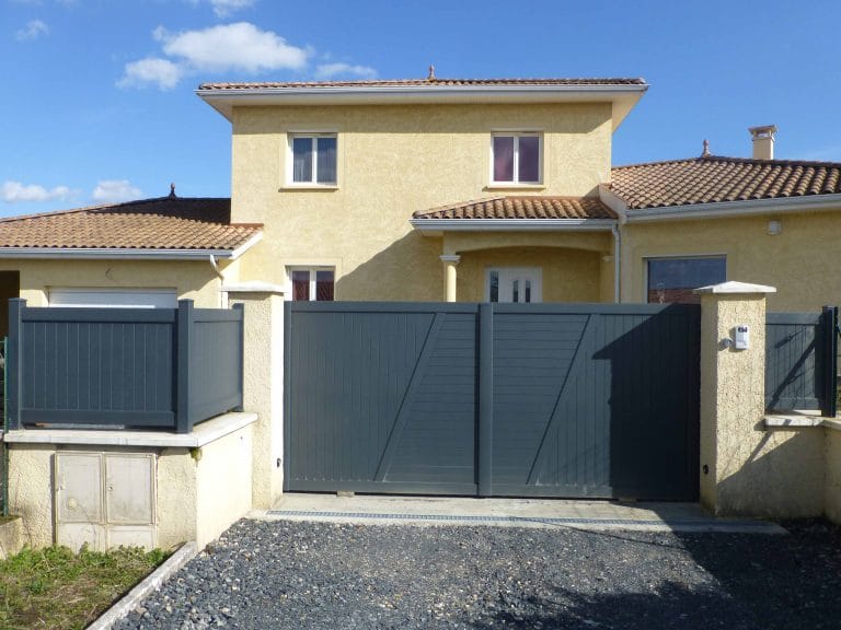 Clôture pleine en aluminium à lames verticales posée sur muret, à côté d'un portail assorti